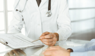 Unknown male doctor and woman-patient discussing current health examination while sitting in clinic and using clipboard. Good medical service in hospital. Medicine concept