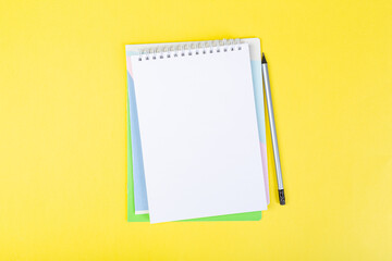 open notepad on yellow background with pencil on top, spiral notepad with blank sheet.