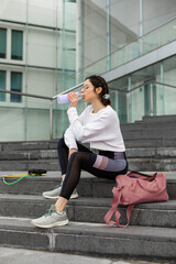 Young sporty woman taking a workout break for drinking water. Urban healthy fitness lifestyle.