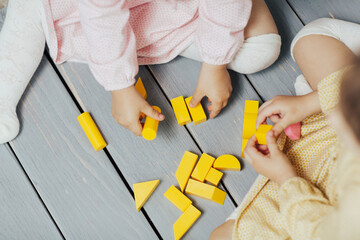 Top view on children's hands playing with colourful yellow blocks on the wooden table background. Learning and education concept. 