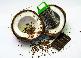 Two split coconut halves with grated chocolate and a small grater.