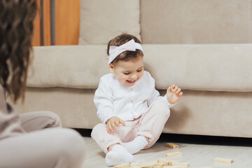Fototapeta premium Smiling baby play with his mother on warm floor with wooden blocks at home.