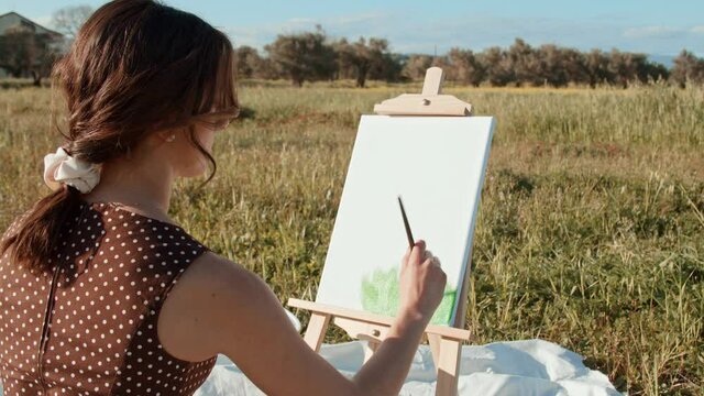Giovane ragazza dipinge su tela un quadro di natura in campagna