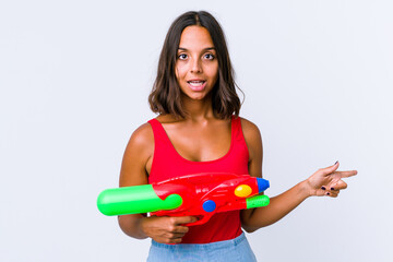 Young mixed race woman holding a water gun isolated excited pointing with forefingers away.