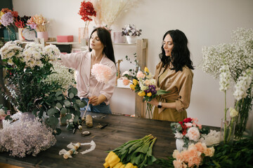 Two young women florist working in flower studio, making beautiful bouquet using fresh plants and...