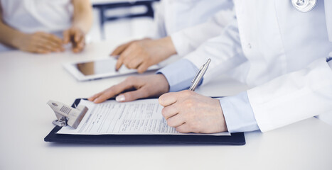 Unknown woman-doctors at work consulting patient. Female physicians filling up medical documents or prescription, close-up. Health care concept