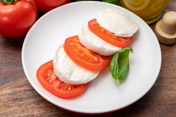 Tasty italian vegetarian food, fresh soft white mozzarella cheese served with red tomatoes and green basil
