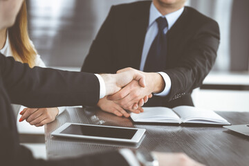 Unknown businessmen shaking hands above the glass desk in a modern office, close-up. Unknown business people at meeting. Teamwork, partnership and handshake concept