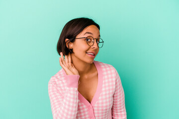 Young mixed race woman isolated on blue background trying to listening a gossip.