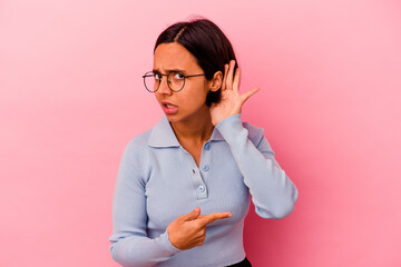 Young mixed race woman isolated on pink background trying to listening a gossip.