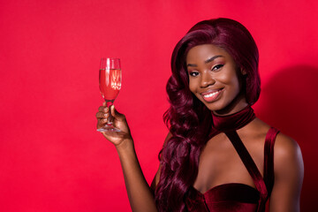 Photo of dark skin charming stunning lady hold glass champagne stand copyspace isolated on red color background