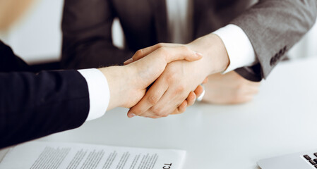 Unknown businessman shaking hands with his colleague or partner above the glass desk in modern office, close-up. Business people group at meeting