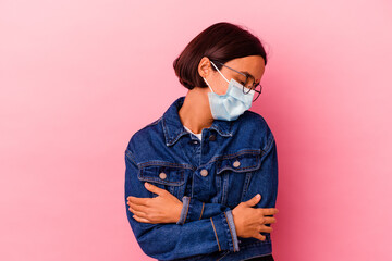 Young Indian woman wearing a mask antivirus isolated on pink background hugs, smiling carefree and...