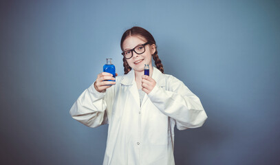 pretty girl with two braids is dressed as scientist and experimenting with blue liquids wearing black glasses in front of blue background