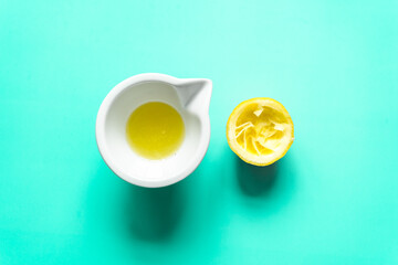 Ein halbierte ausgepresste Zitrone und Zitronensaft in einer weißen Schüssel. Draufsicht, minzgrün Hintergrund.