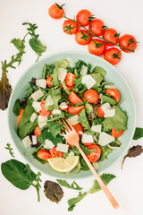 Mediterranean salad with cherry tomatoes, spinach and greenery. Healthy fresh salad of vegetable, tomatoes, spinach, arugula in a green plate on a white background. Top view. 