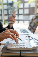 Savings, finances, economy and home concept - close up of businesswoman with calculator counting money and making notes at home office