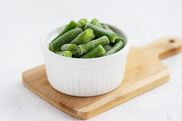 Frozen green beans in a bowl on a wooden board.