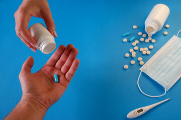 Medicine and healthcare concept. The woman gives the capsule to the man. Capsules, pills, medical mask on a blue background. Place for your text.