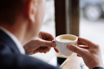 A man in a business suit holds a cup of hot coffee in his hands. Morning businessman in cafe .Copy...