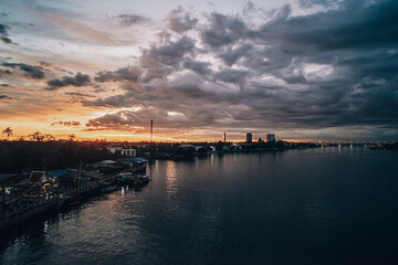 Fototapeta na wymiar Panorama Cityscape at sunset with large river at foreground and strom clouds at background in Thailand.