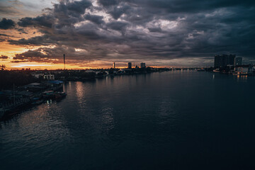 Panorama Cityscape at sunset with large river at foreground and strom clouds at background in Thailand.