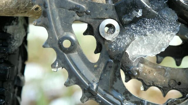 Water drips down from MTB crankset teeth. Melting snow on metal during a bike trip break.