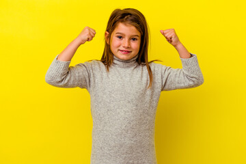 Little caucasian girl isolated on yellow background showing strength gesture with arms, symbol of...