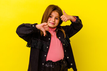 Little caucasian girl isolated on yellow background showing thumbs up and thumbs down, difficult...