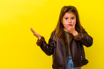 Little caucasian girl isolated on yellow background holds copy space on a palm, keep hand over...