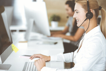 Blonde business woman using headset for communication and consulting people at customer service office. Call center. Group of operators at work