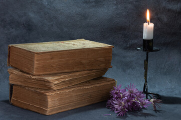 a stack of old books on the table and a burning candle