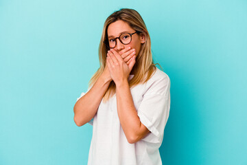 Young mixed race woman isolated on blue background covering mouth with hands looking worried.