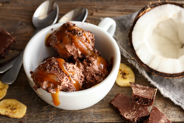 Chocolate coconut vegan ice cream in a white cup. Ice cream balls with chocolate and caramel. Wooden background, copy space.