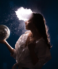 young woman in a club of smoke and soap bubbles holds a shiny disco ball in her hand