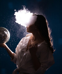 young woman in a club of smoke and soap bubbles holds a shiny disco ball in her hand