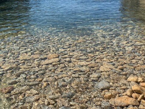 Sea transparent water, crystal clear sea water surface on pebbles beach. Zen landscape, mediation of nature, beautiful seascape, sunlight on stones.