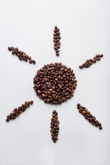 Sun sign made of dark roasted coffee beans on white aquarelle paper background