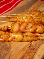 Marinated raw chicken pieces on a wooden skewer. Summer barbeque range product. Asian style sous over poultry meat. Red and white classic table cloth
