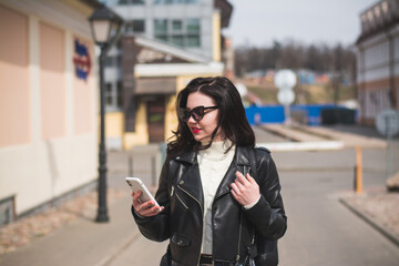 Fototapeta premium A beautiful hipster girl with a phone in her hands walks down the street
