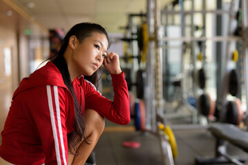 Serious Asian rebel woman thinking and sitting at gym