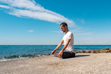 Attractive young man practicing yoga meditation and breathwork outdoors by the sea