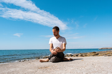 Attractive young man practicing yoga meditation and breathwork outdoors by the sea