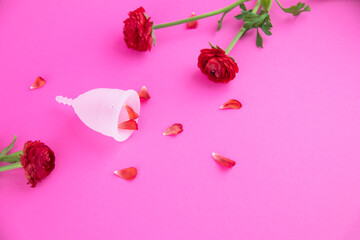 White eco-friendly menstrual cup on a pink background with red flowers as a symbol of blood. Female hygiene during the menstrual cycle. Ecological and reusable.