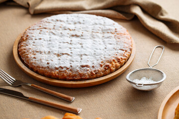 Sweet fresh baked pie with powdered sugar on a wooden board