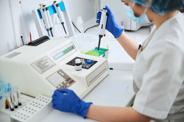 Scientist in a mask preparing a laboratory tool for pipetting