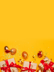 Top view of holiday card with gold brown eggs and gift boxes with red ribbon bow and glitter confetti on a yellow background.Happy easter.