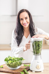 Good looking girl ina home kitchen preparing healthy raw food in a form of green smoothie