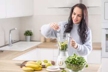 Woman adds water into a mixer for a spinach, banana, and apple smoothie