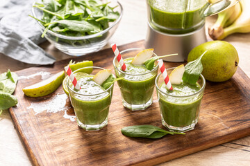Cups of green smoothie with colorful paper straws and wedges of lime on a table